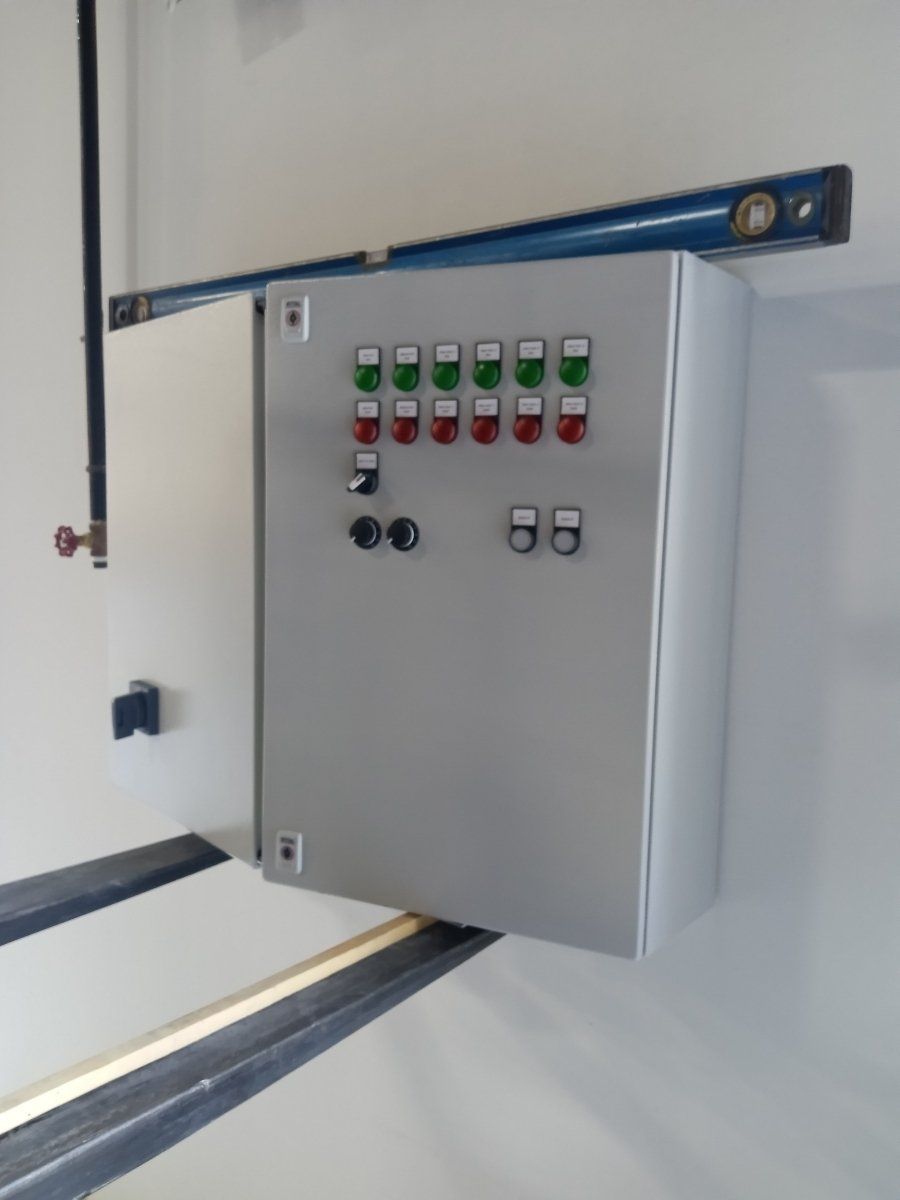 Silver control panel with green and red lights, mounted on a white wall. A level rests on top.