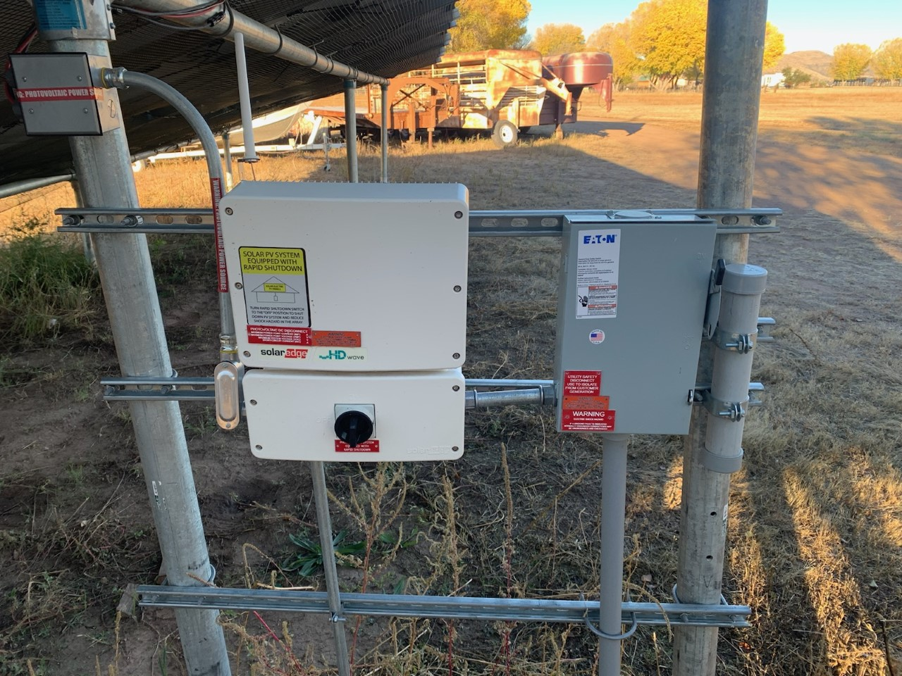 Solar panel inverters and electrical components mounted on metal framework in a rural setting.