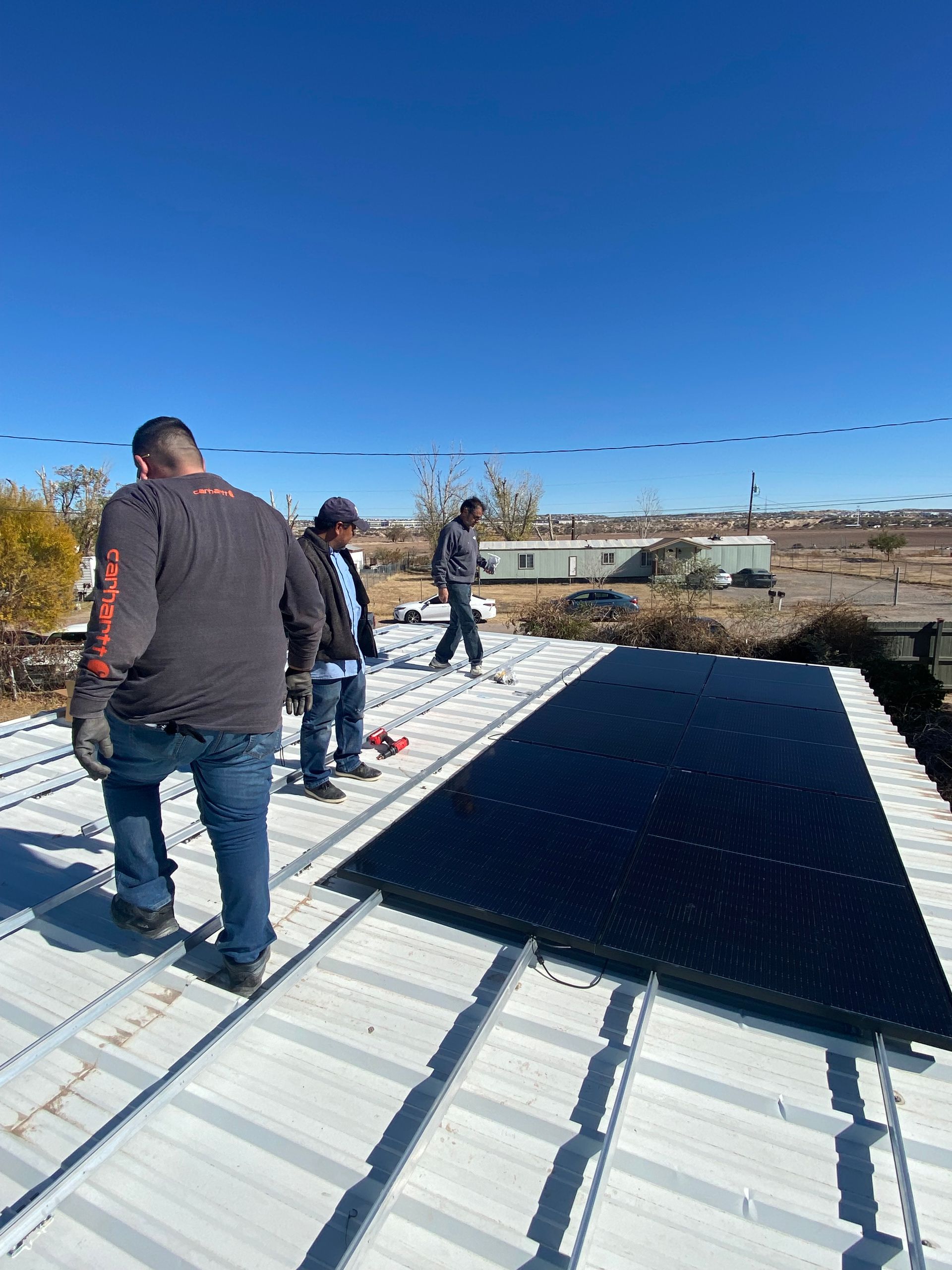 Three workers installing a solar panel on a metal roof under a blue sky.