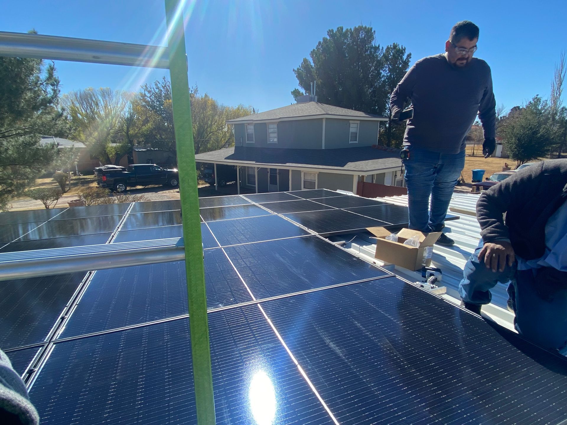 Workers installing solar panels on a roof, sunny day, blue sky, two-story house in background.
