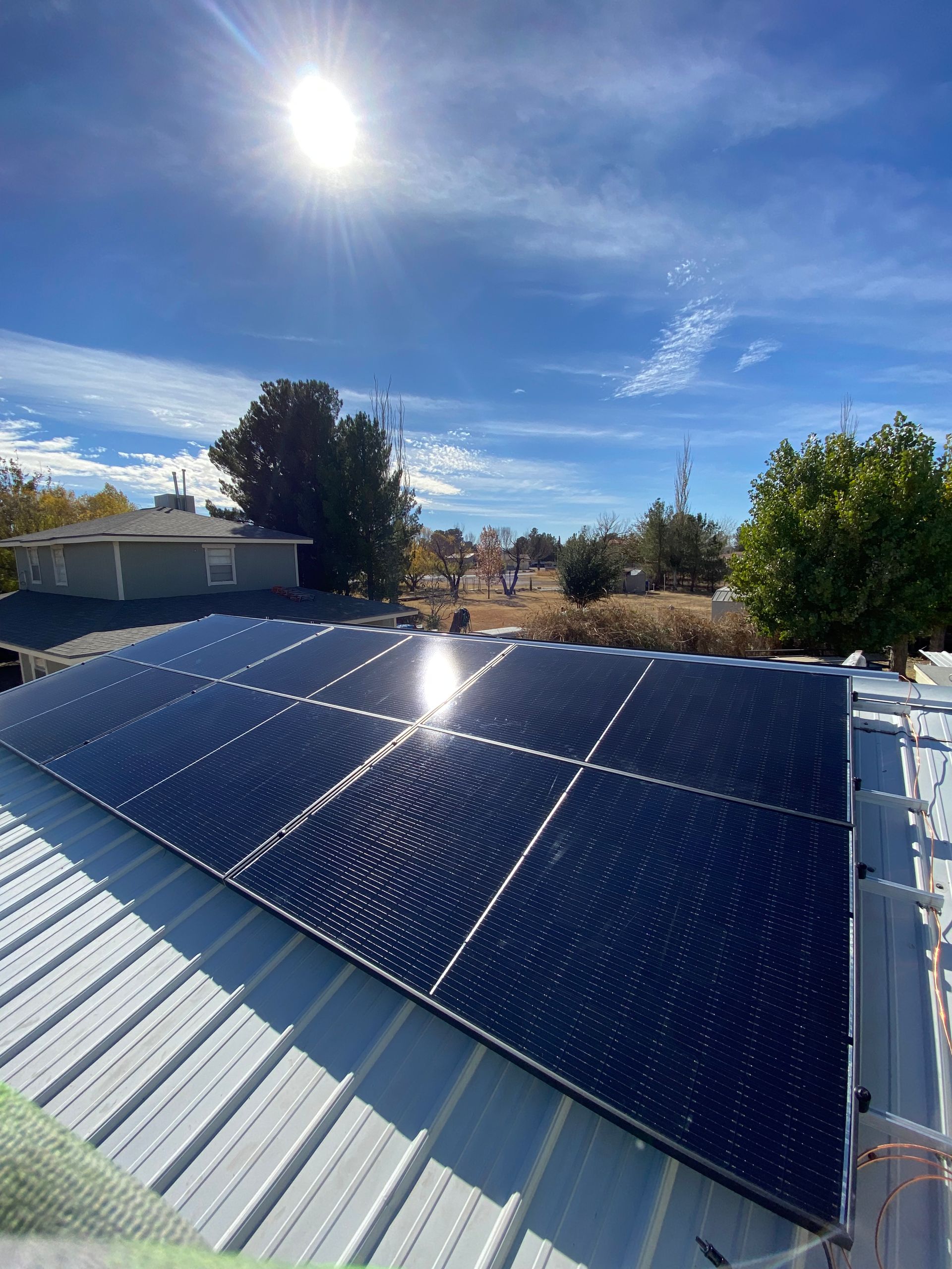 Solar panels on a metal roof, reflecting sunlight under a blue sky.