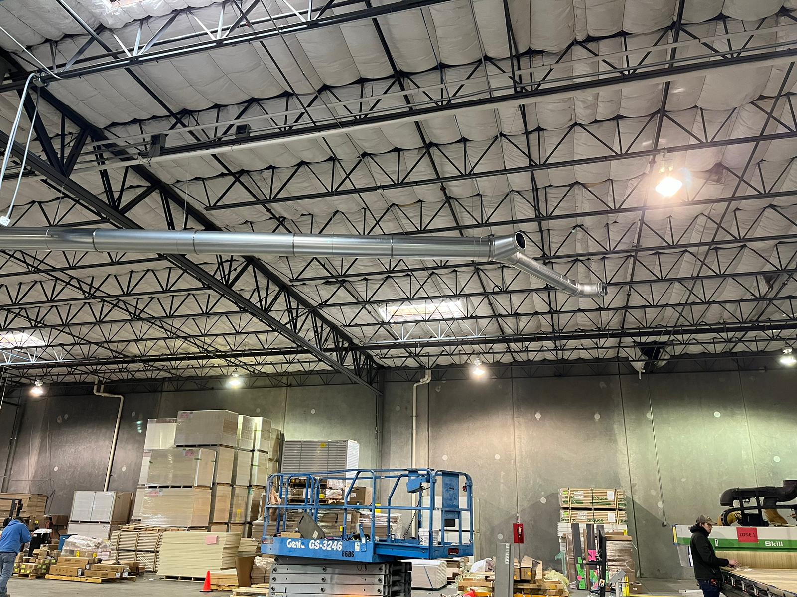 Interior view of a warehouse construction. Black trusses, gray walls, and a blue lift are visible.