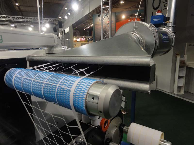 A machine winding a blue mesh filter with a gray metal housing in an industrial setting.
