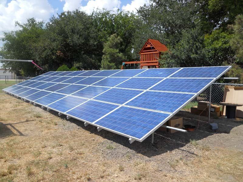 Solar panels in a yard, angled toward the sky, with a playground in the background.