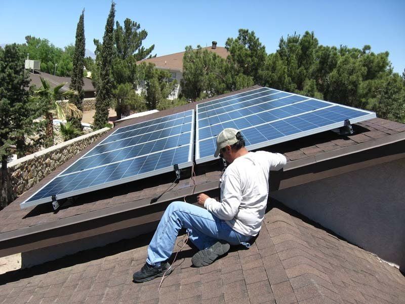 Man on roof installing solar panels. Sunny day, residential area.