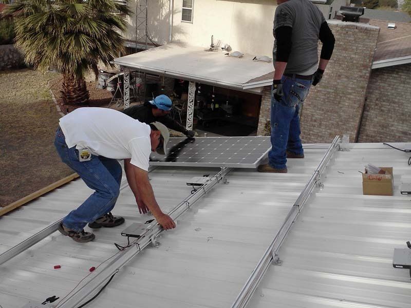 Solar panel installation: workers on a roof, placing panels onto rails.