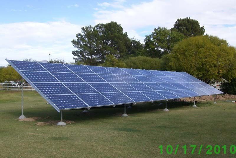 Solar panels installed outdoors on a grassy lawn with trees and a cloudy sky.
