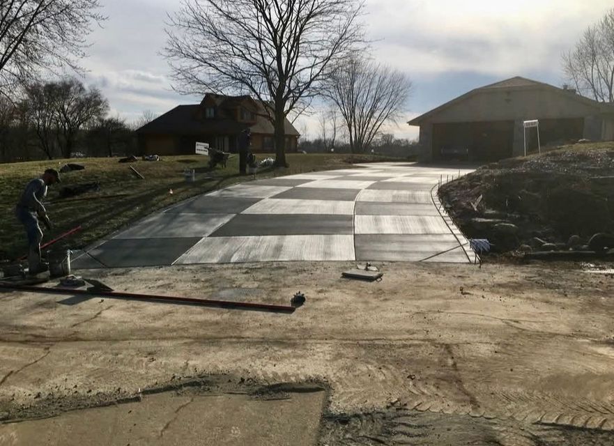 Road under repair with fresh concrete slabs, two workers, and houses in the background