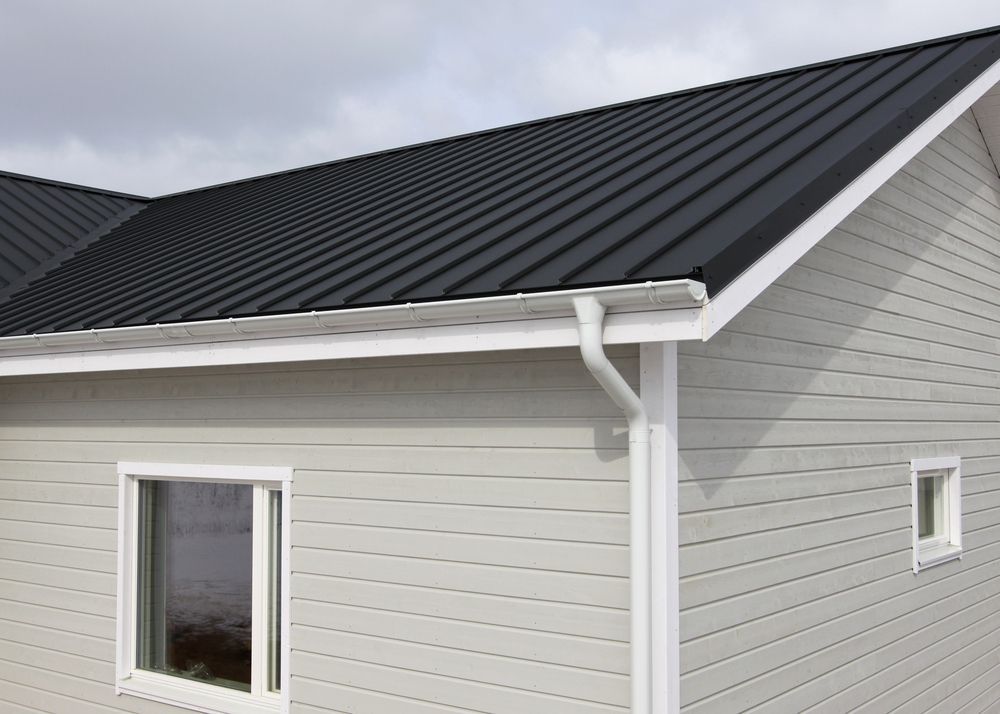 House with a black metal roof, white siding, and gutters. Two windows visible. Overcast sky. — McLuckie Metal Roofing In St George, NSW