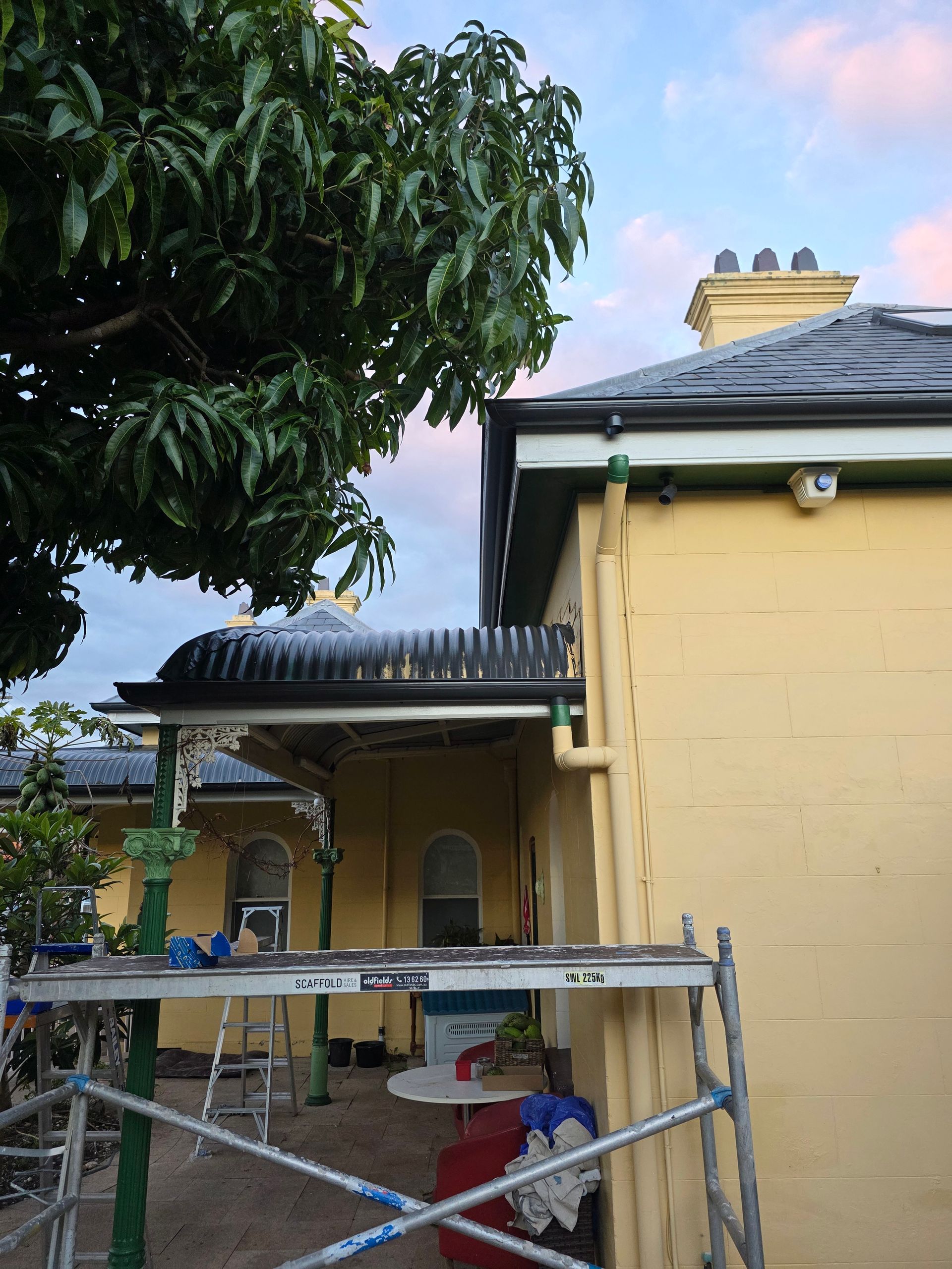 Yellow Building With Dark Roof, Green Tree, Scaffolding — McLuckie Metal Roofing In Lugarno, NSW