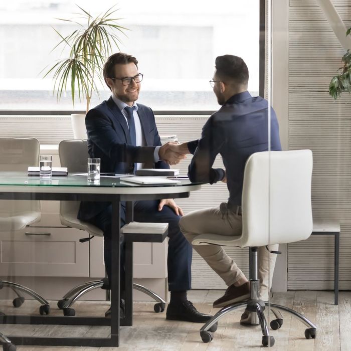 Two men are shaking hands while sitting at a table.