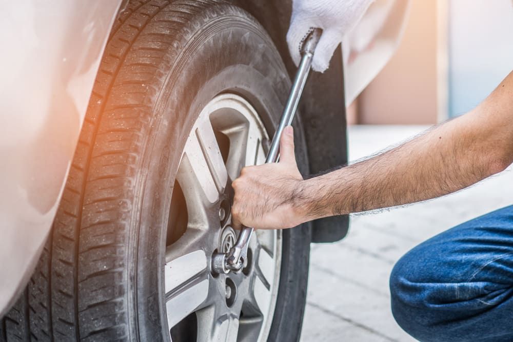 A Man Is Changing A Tyre On A Car With A Wrench — Tyrepower Innisfail In Cardwell, QLD