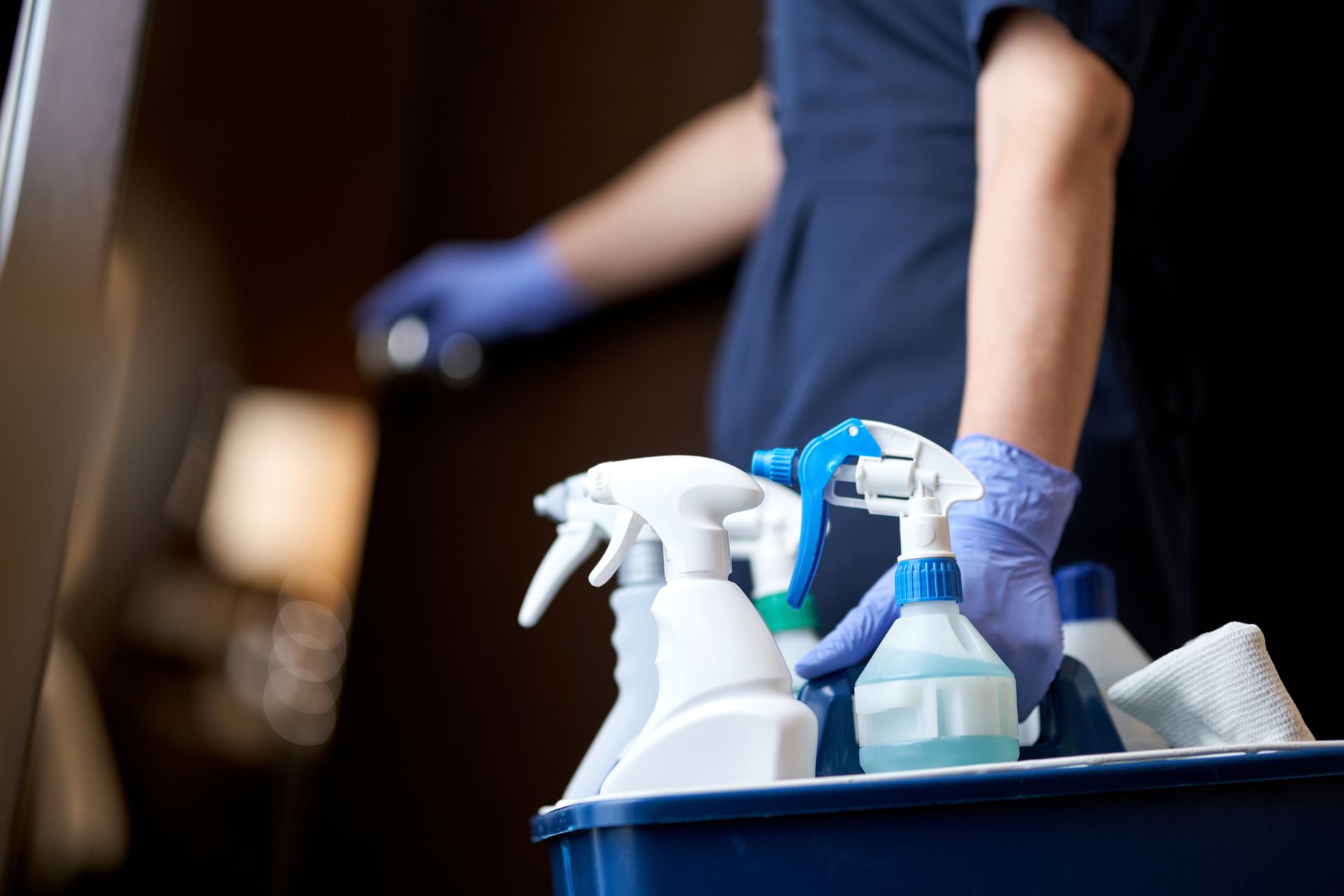 Cleaning cart with spray bottles as a gloved worker opens a door. Cleaning cart with spray bottles as a gloved worker opens a door.
