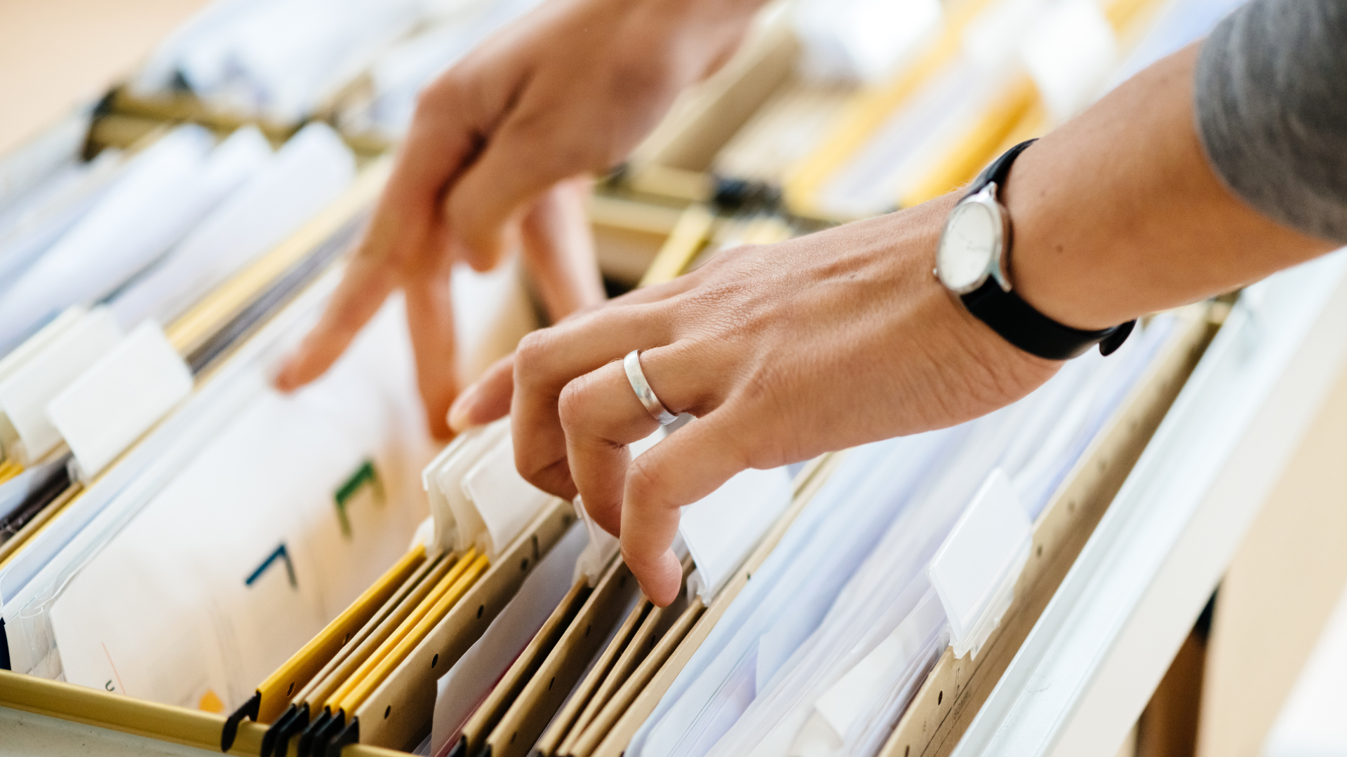 Hands sorting through files in a filing cabinet, searching for a document.