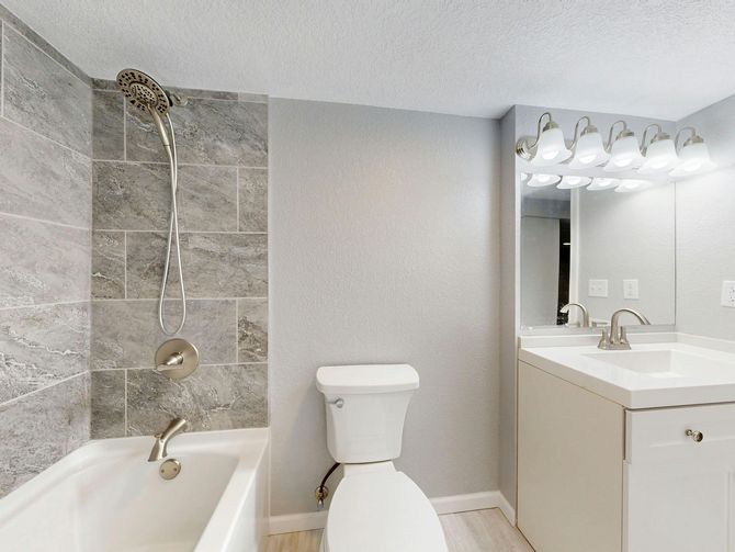 Bathroom with gray tile shower, white toilet, vanity, and neutral-colored walls.
