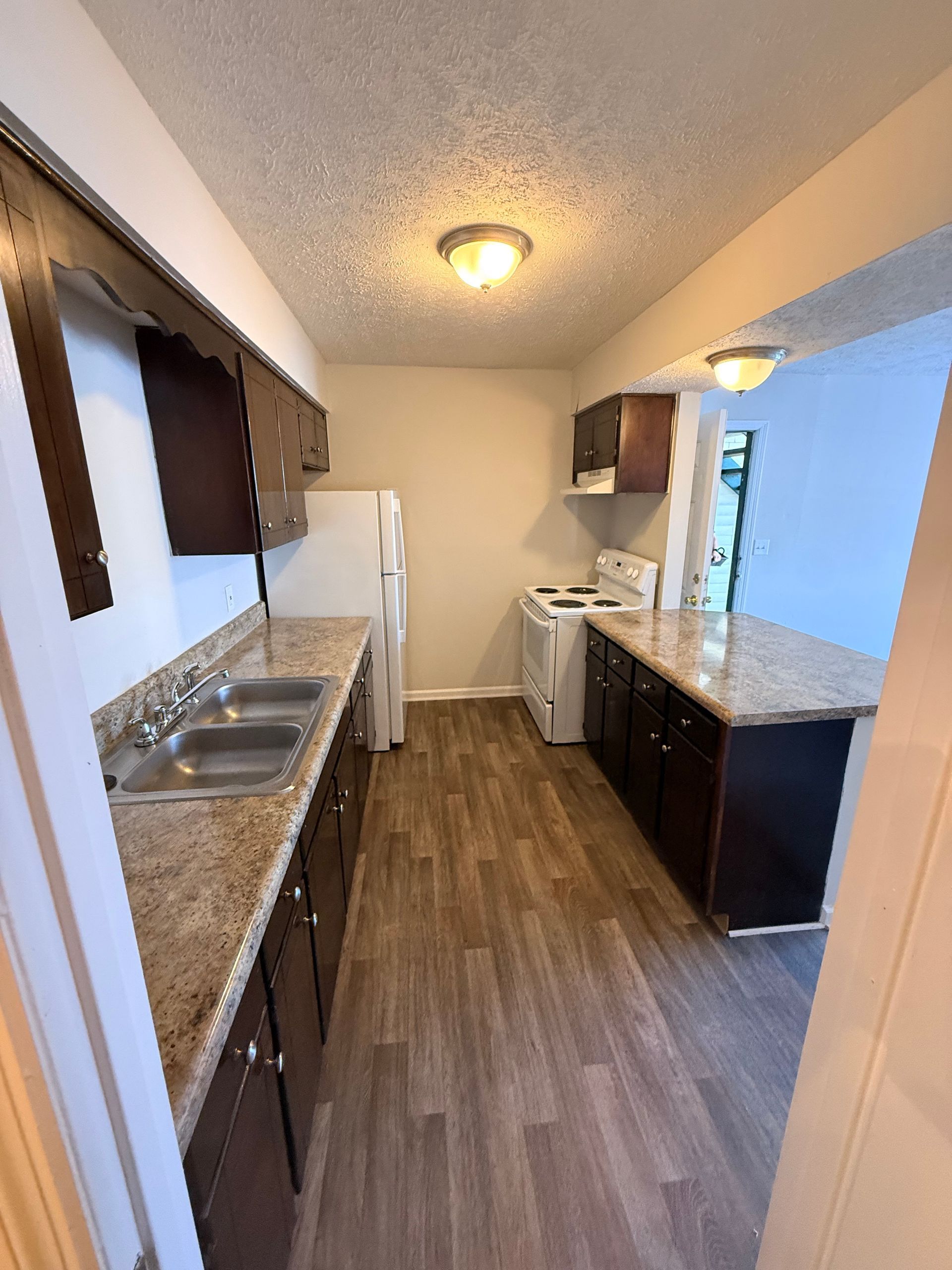 Narrow galley kitchen with granite counters, white cabinets, and wood flooring seen from the doorway