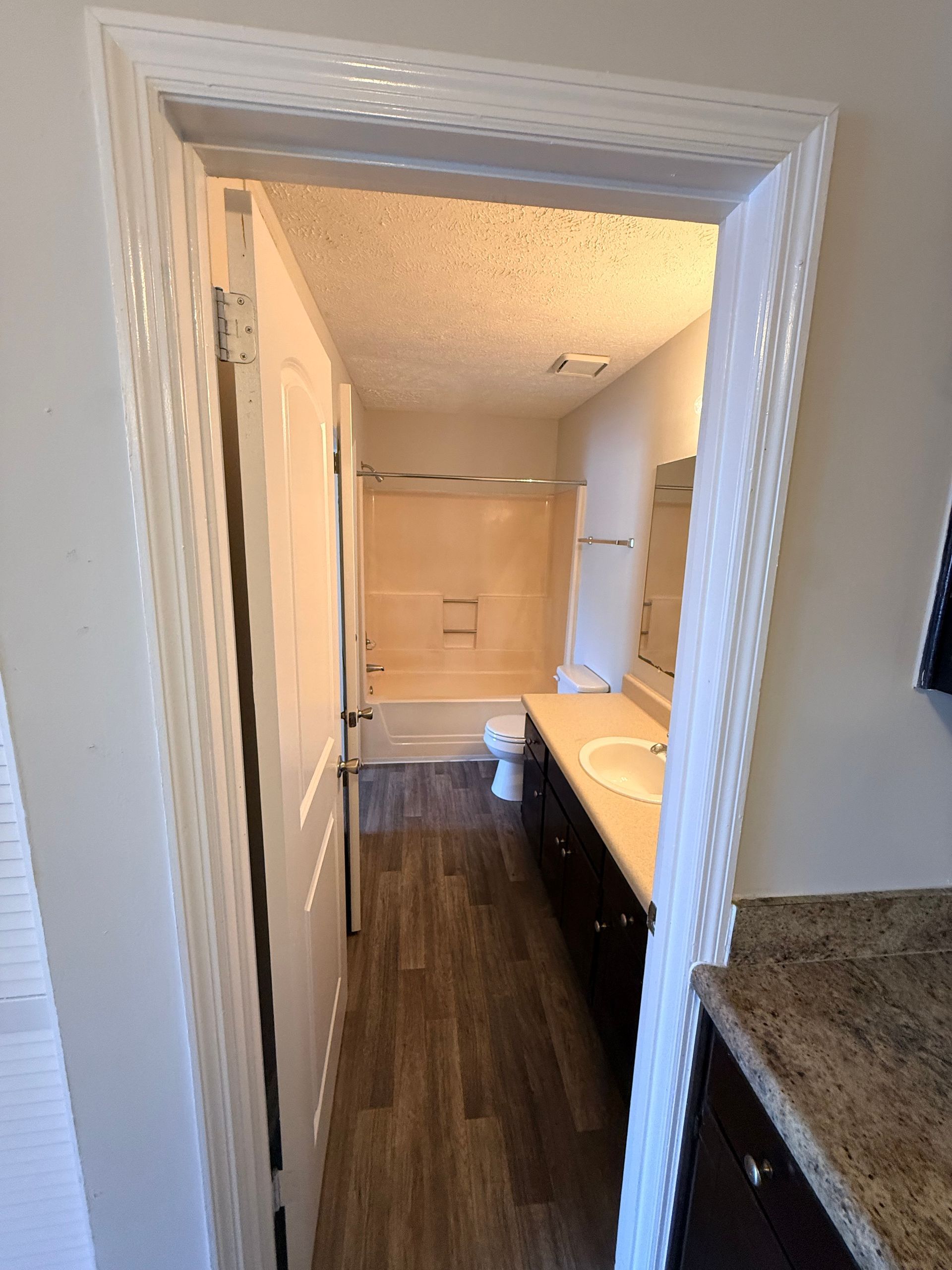 Bathroom vanity seen through a doorway, with white cabinets, beige sink, and dark wood floor.