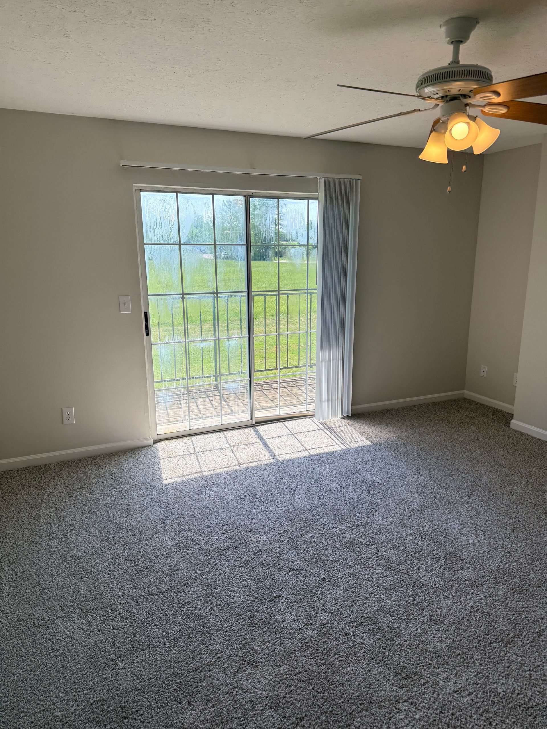 Empty carpeted room with sliding glass doors, light gray walls, and a ceiling fan with light.