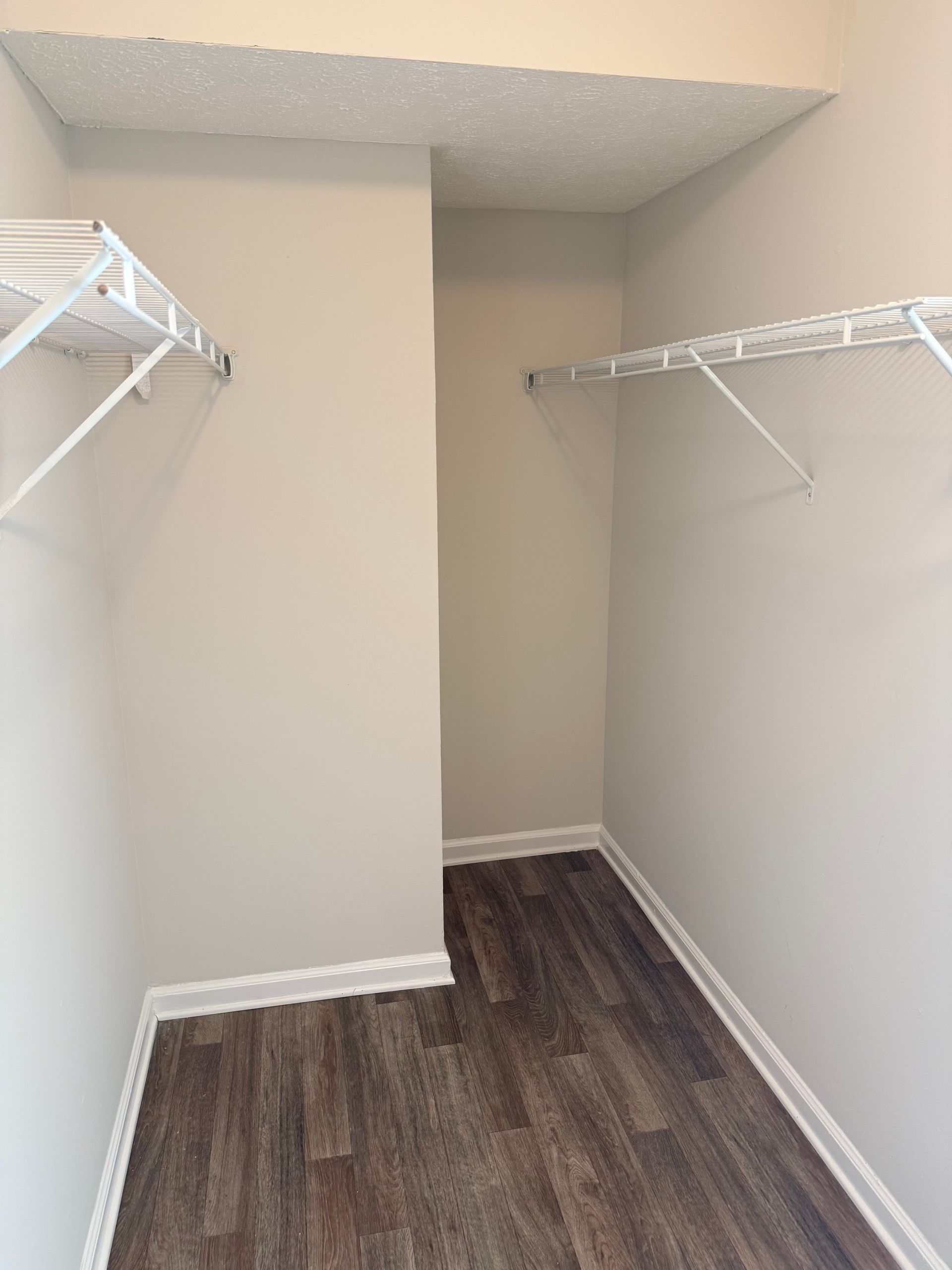 Empty walk-in closet with white walls, wire shelves, and dark wood-look flooring