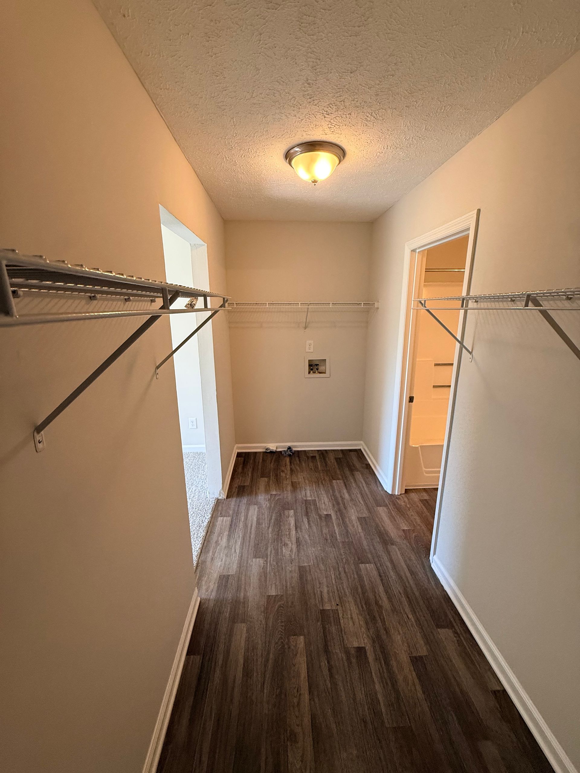 Empty walk-in closet with wire shelving, brown floor, and a ceiling light.
