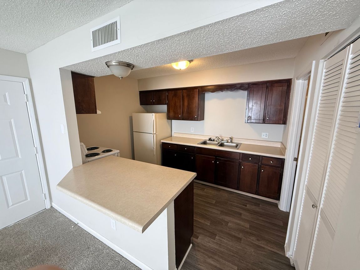 Small kitchen with a beige island, dark wood cabinets, white appliances, and louvered closet doors.