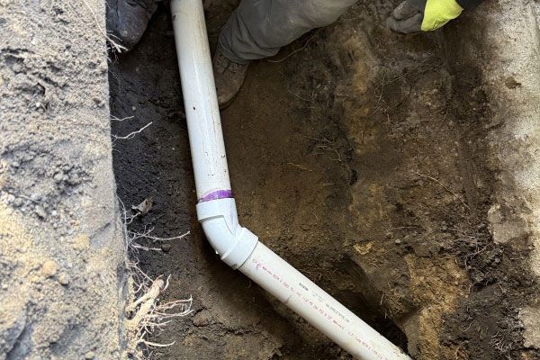 PVC pipe in an excavated dirt trench with a purple coupling and gloved hands nearby