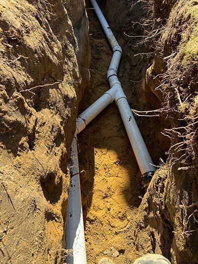 Exposed gray PVC pipes running through a narrow dirt trench during underground utility installation