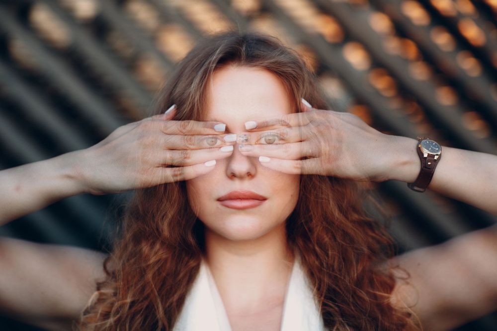 Una donna si copre gli occhi con entrambe le mani, sullo sfondo sfocato e decorato.