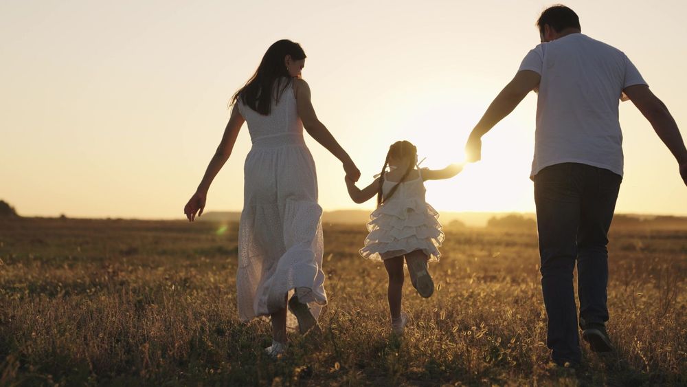 Una famiglia che si tiene per mano mentre passeggia in un campo al tramonto.