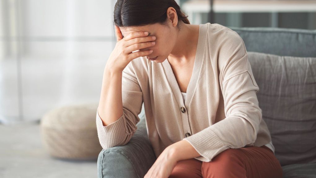 Donna seduta su un divano con la mano a coprirle il viso, dall'aspetto stressato o turbato.