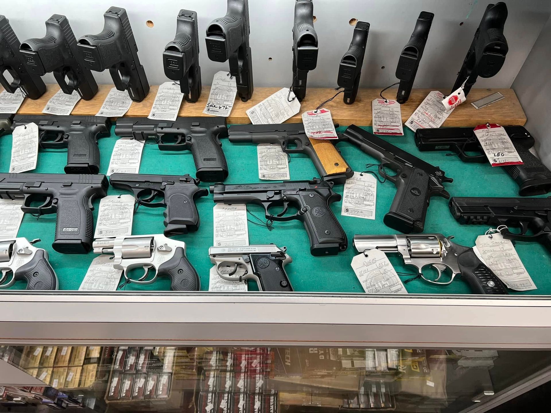 Gun display case with multiple handguns arranged on shelves, each tagged with price labels.
