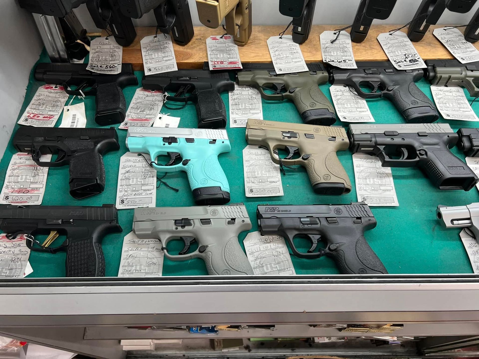 Display case with multiple handguns arranged on green felt at a gun shop or showroom