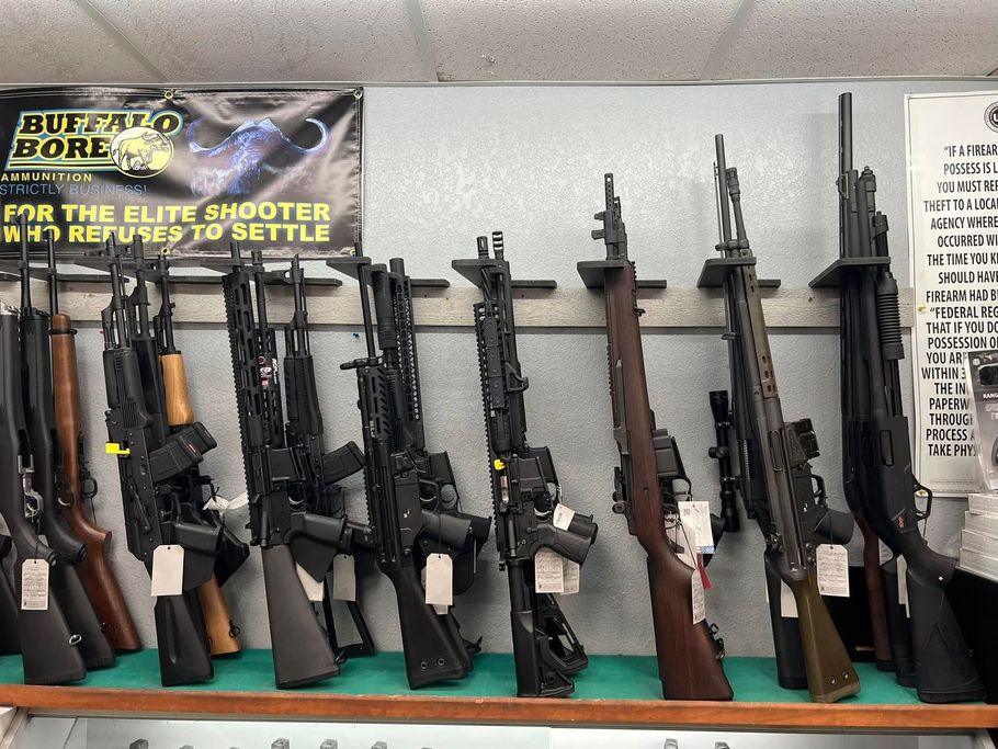 Assault rifles displayed upright on a store wall beneath a “Bullets for the elite shooter” sign.
