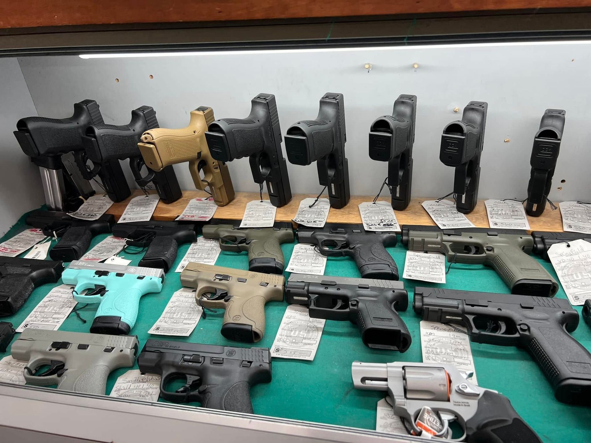 Assorted handguns displayed in rows on a counter, with black, tan, and silver finishes.
