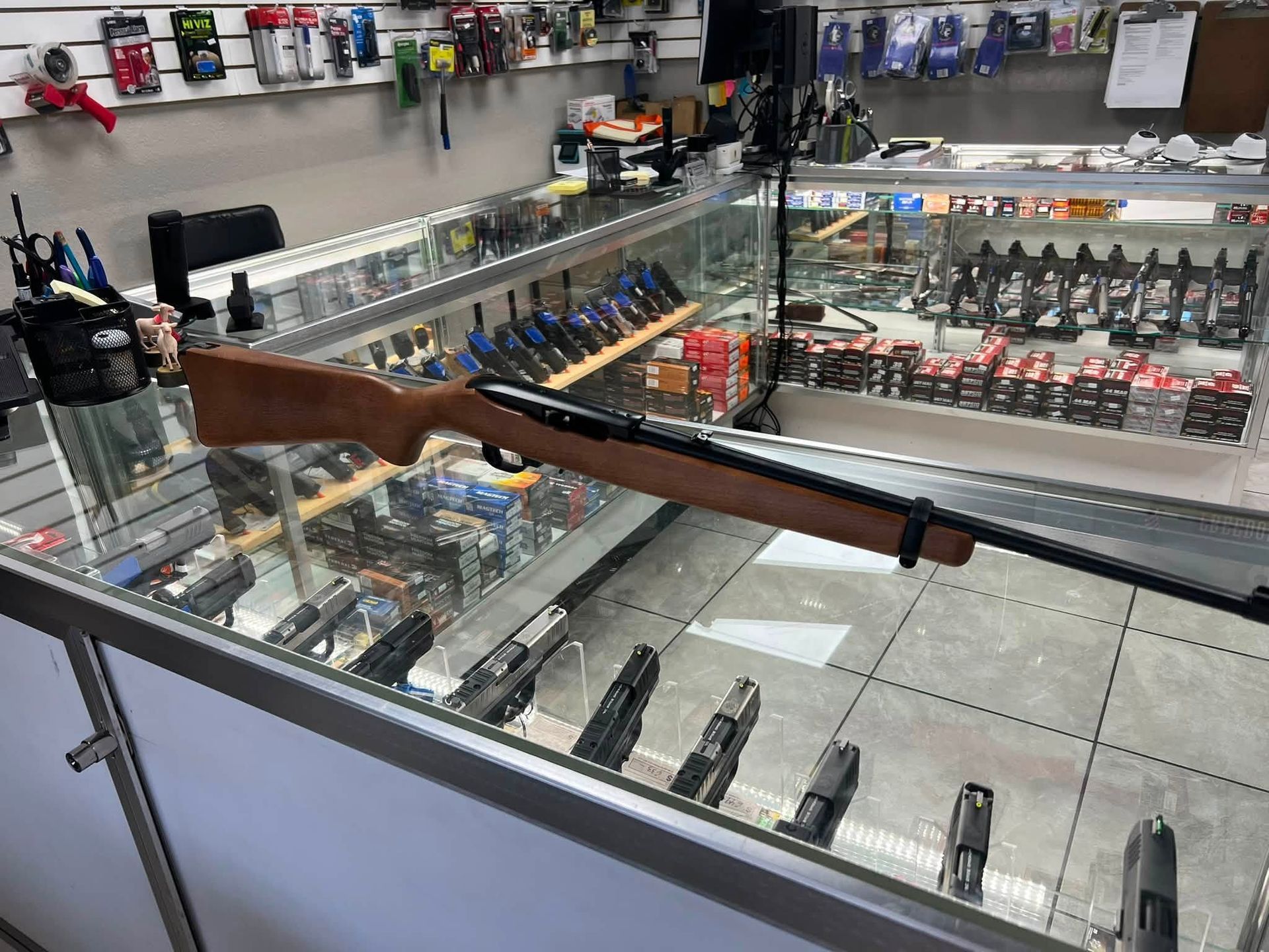 Rifle displayed across a glass display case in a gun shop interior.