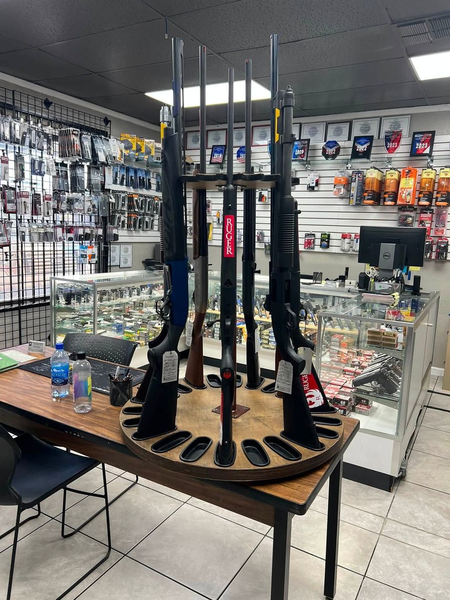 Gun display case in a store, with rifles and accessories on a round wooden table.