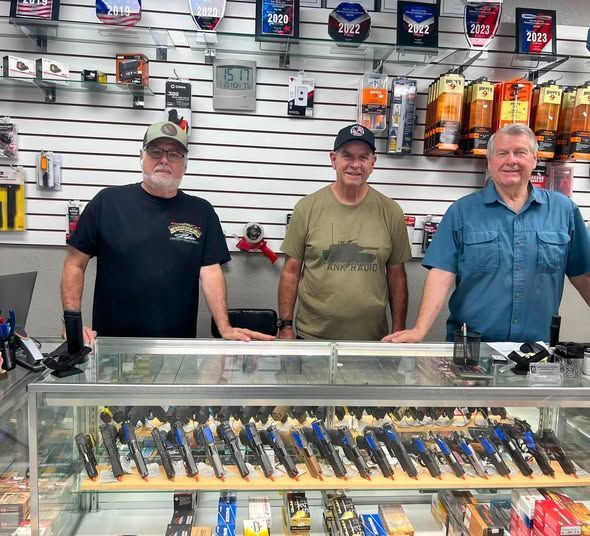 Three men standing behind a gun display counter in a shop