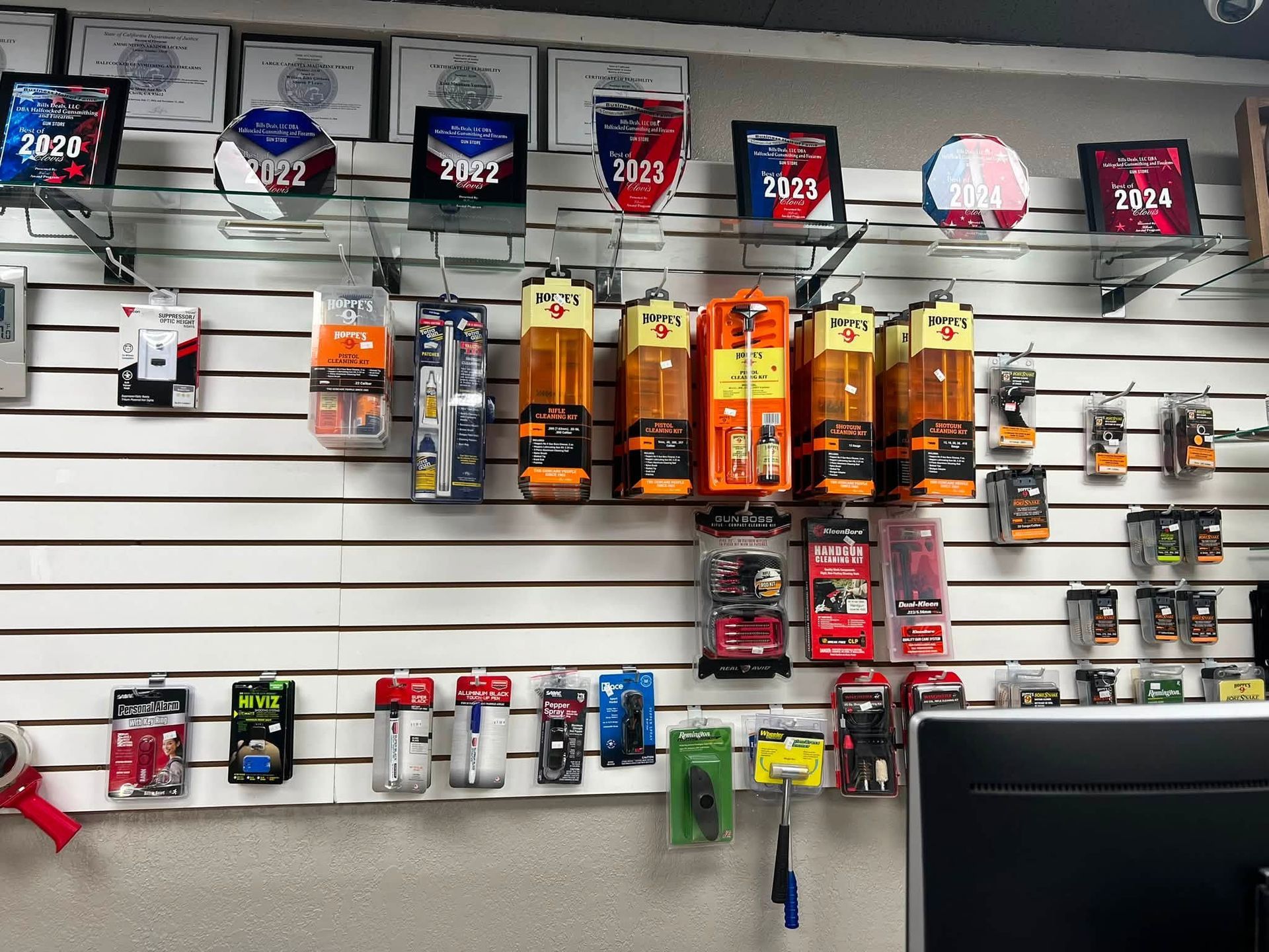 Display wall of sports memorabilia and cards on slatwall shelves in a shop; monitor at bottom right