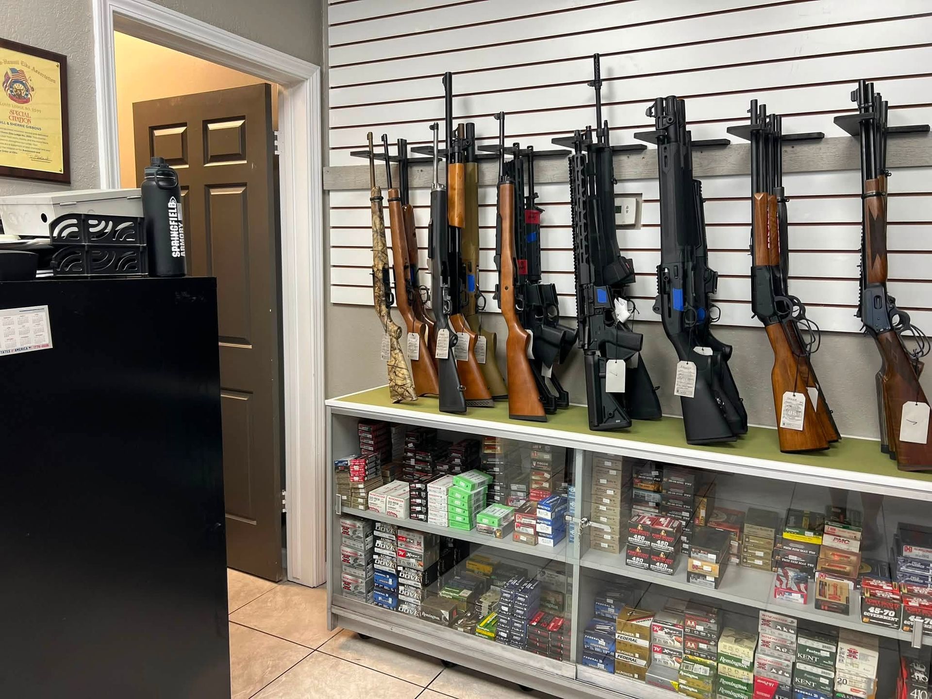 Gun display in a store, with rifles on wall racks and ammunition under glass shelves.