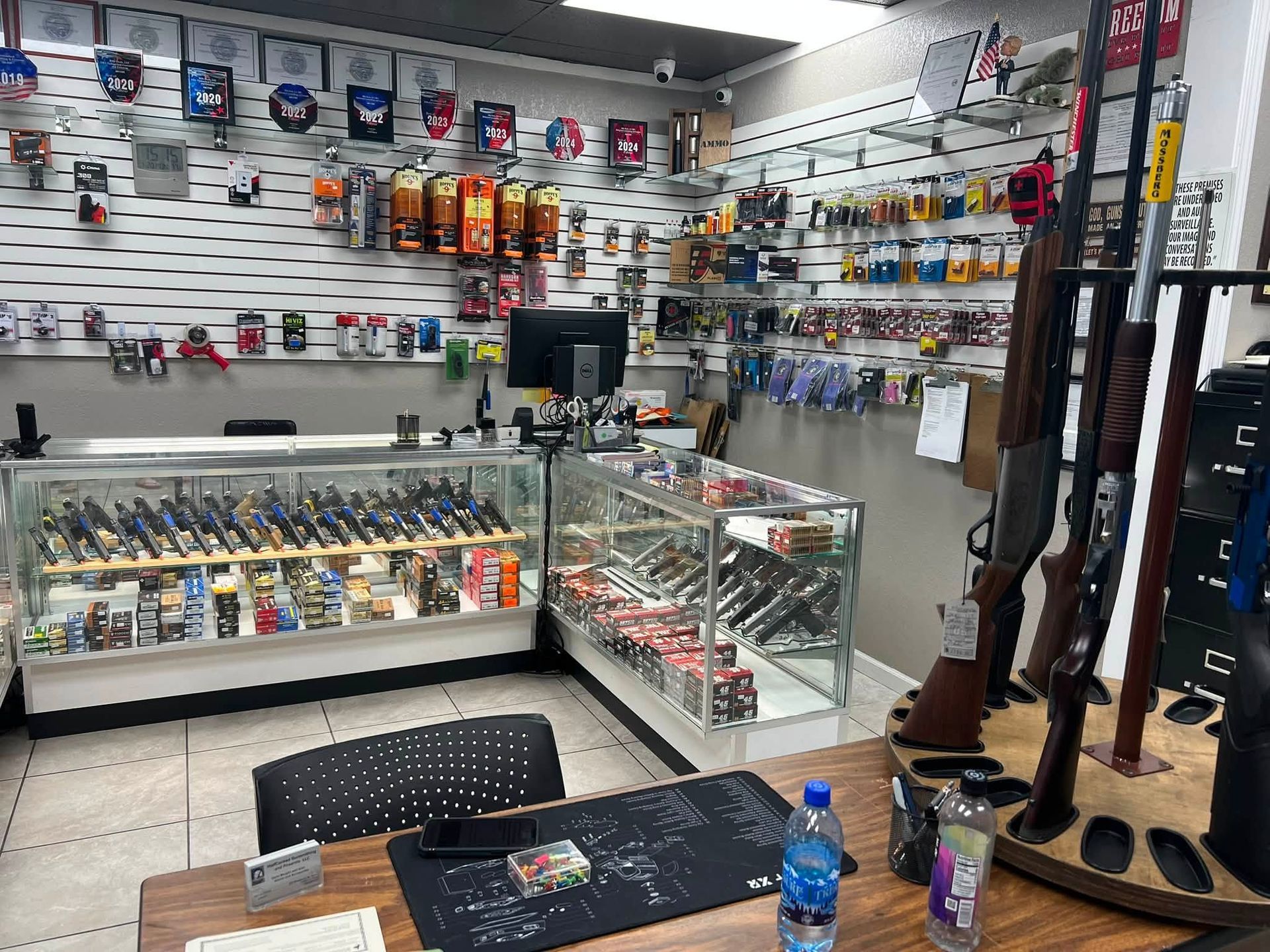 Gun store interior with firearms on wall racks and display cases, viewed from a counter