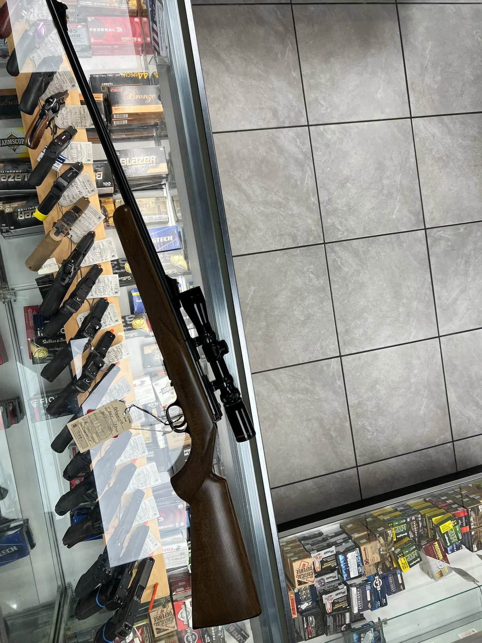 Two black rifles with tags leaning on a green table against a gray wall
