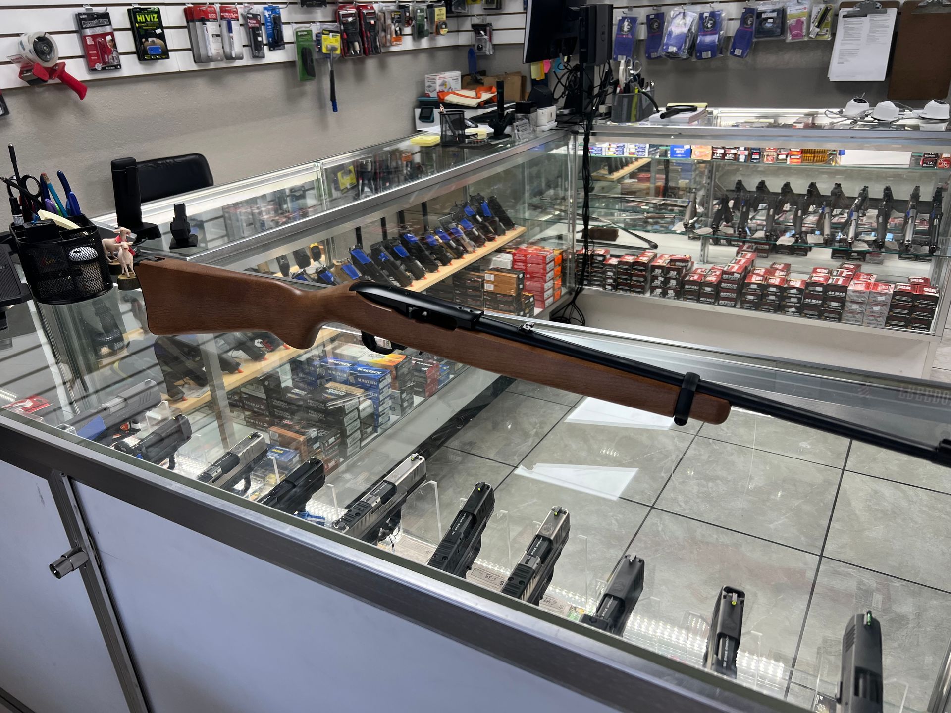 Three men standing behind a display case in a gun shop, with firearms on the wall behind them.