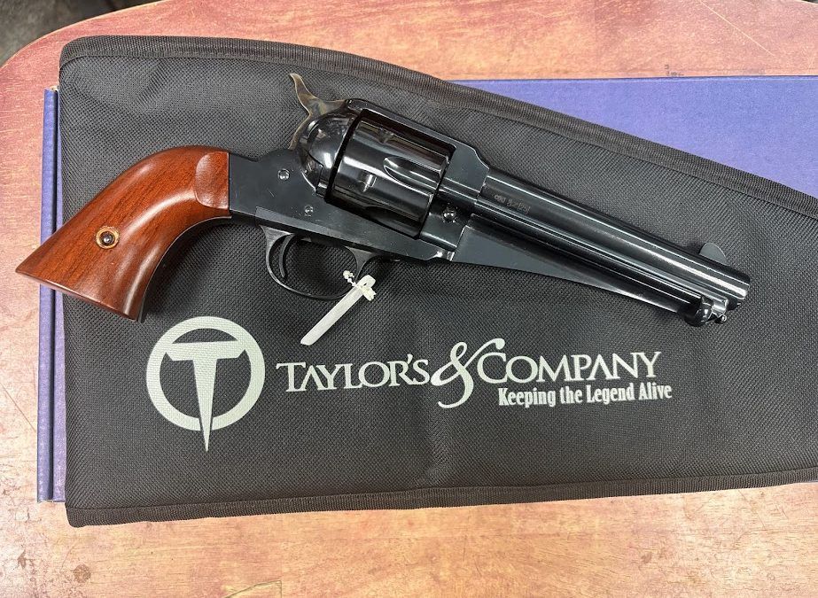 Revolver with wooden grip on a Taylor's & Company gun case, photographed on a table.