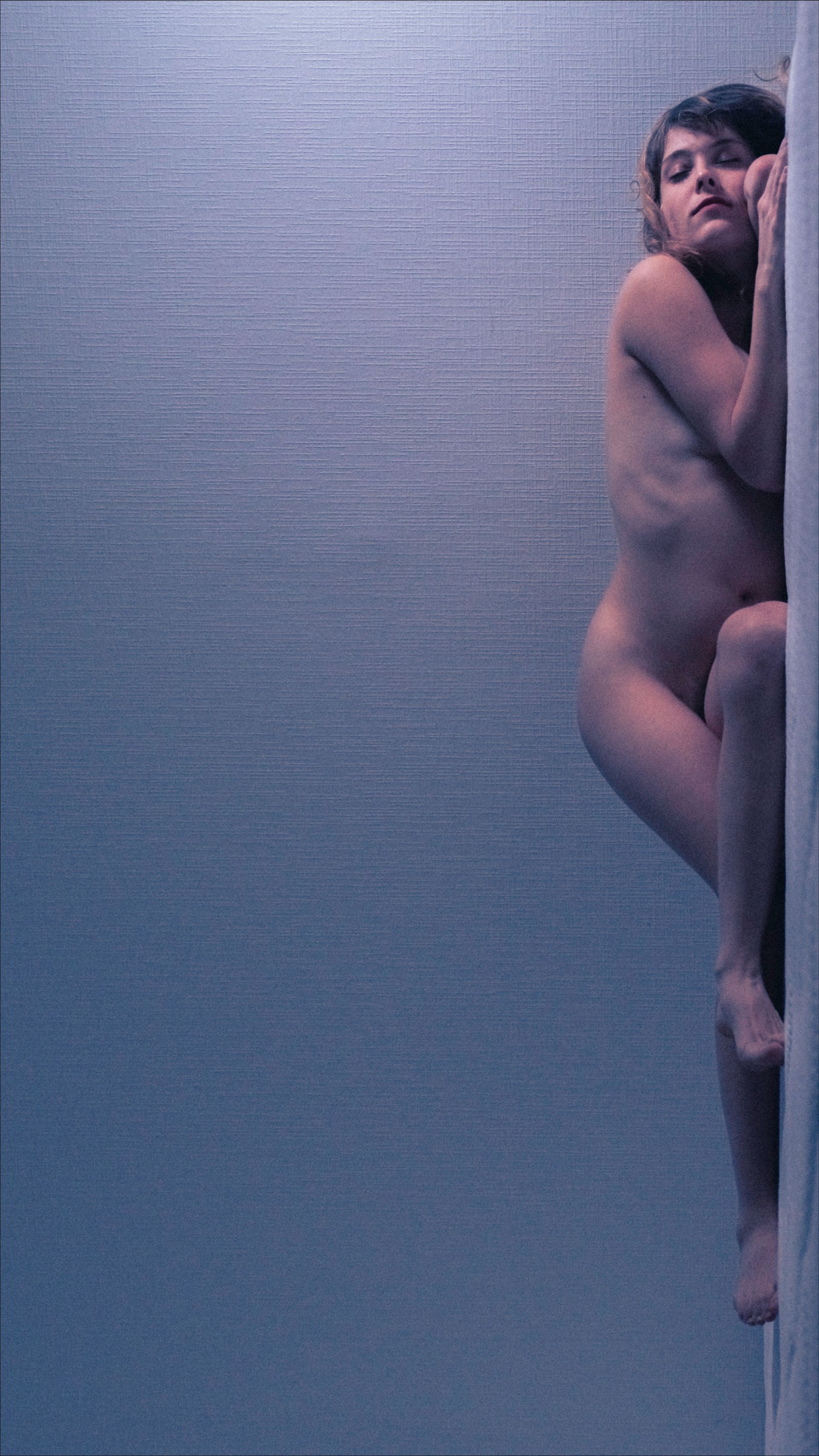 Nude person clinging to a vertical surface with arms and legs, blue toned.