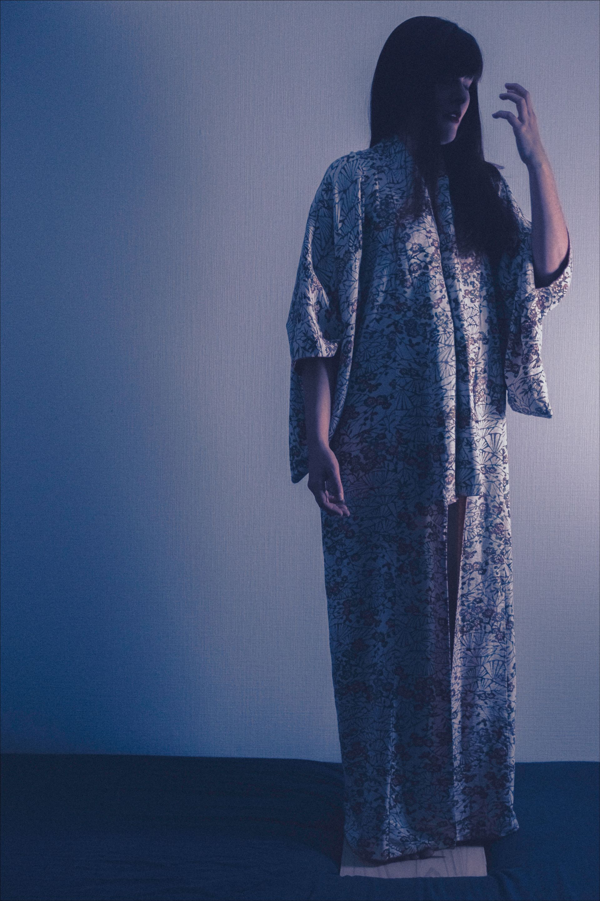 Person in shimmery robe and pants, standing in front of a blue wall, hand in hair.