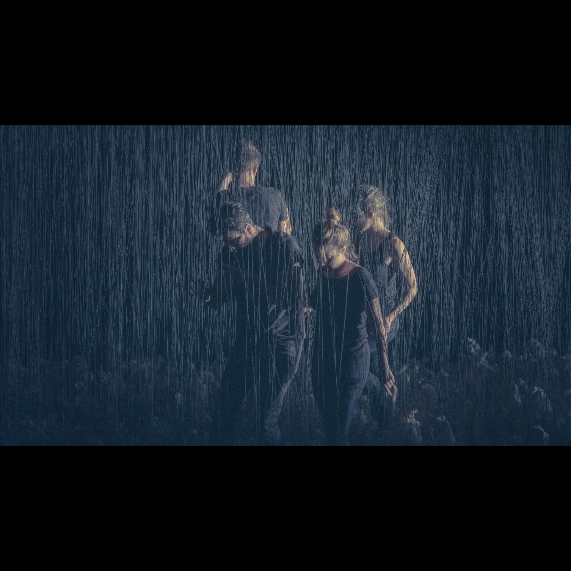 People walking in heavy rain. Dark clothing, blue-toned environment.