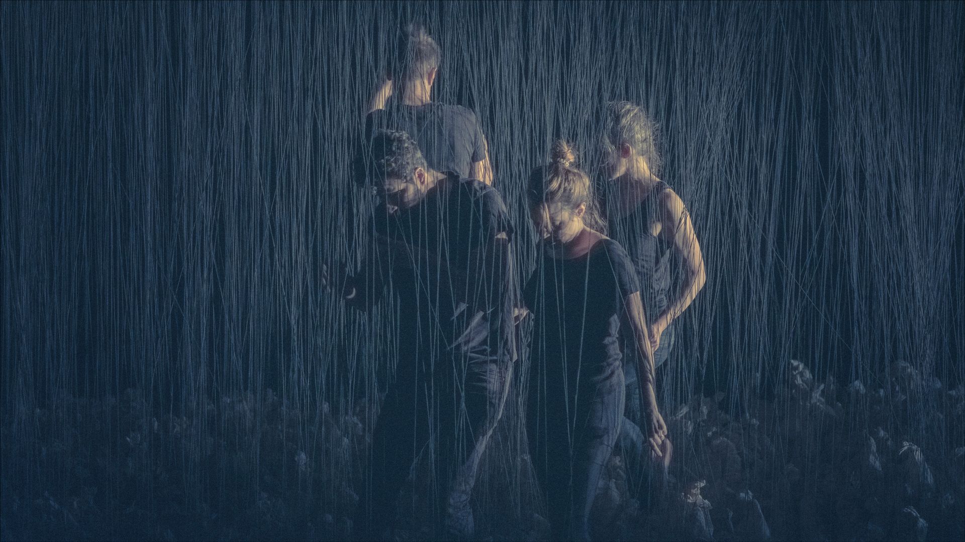 Four people in dark clothing in heavy rain, partially obscured.
