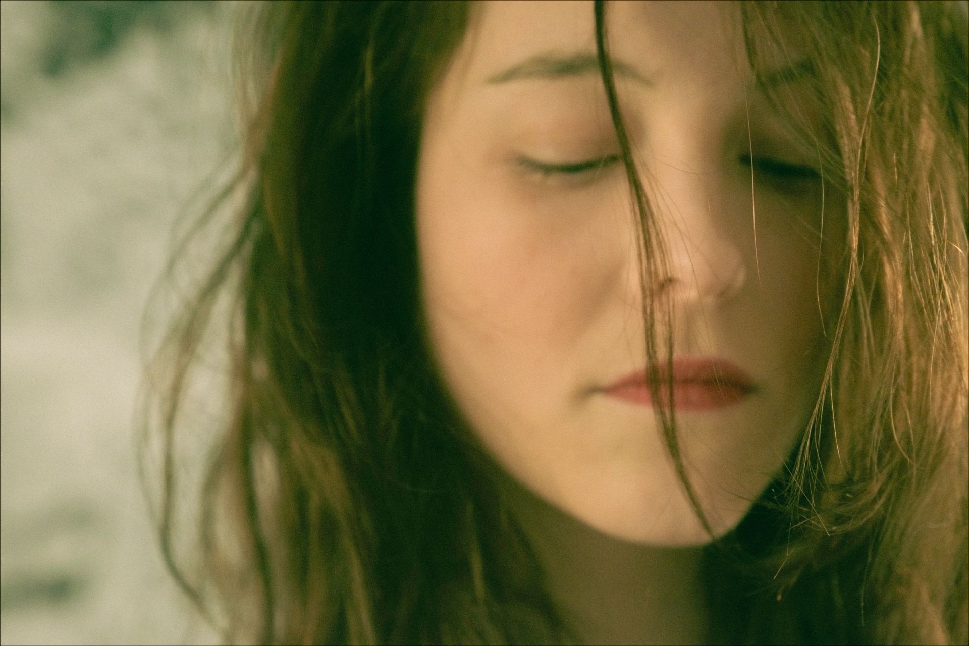 Woman with closed eyes, soft expression, and wind-blown brown hair; close-up shot.