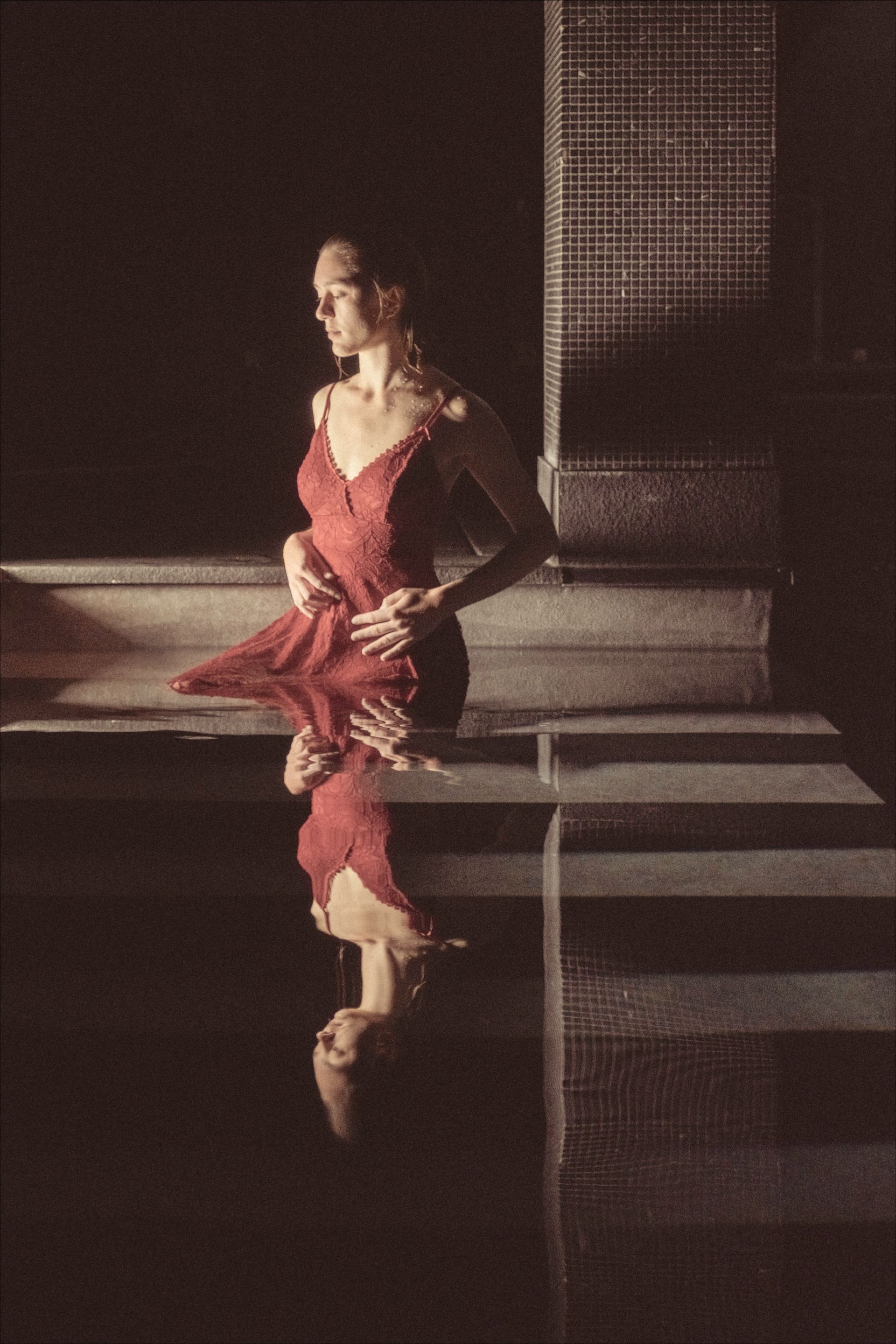Woman in red dress by water, reflected image, dark setting.