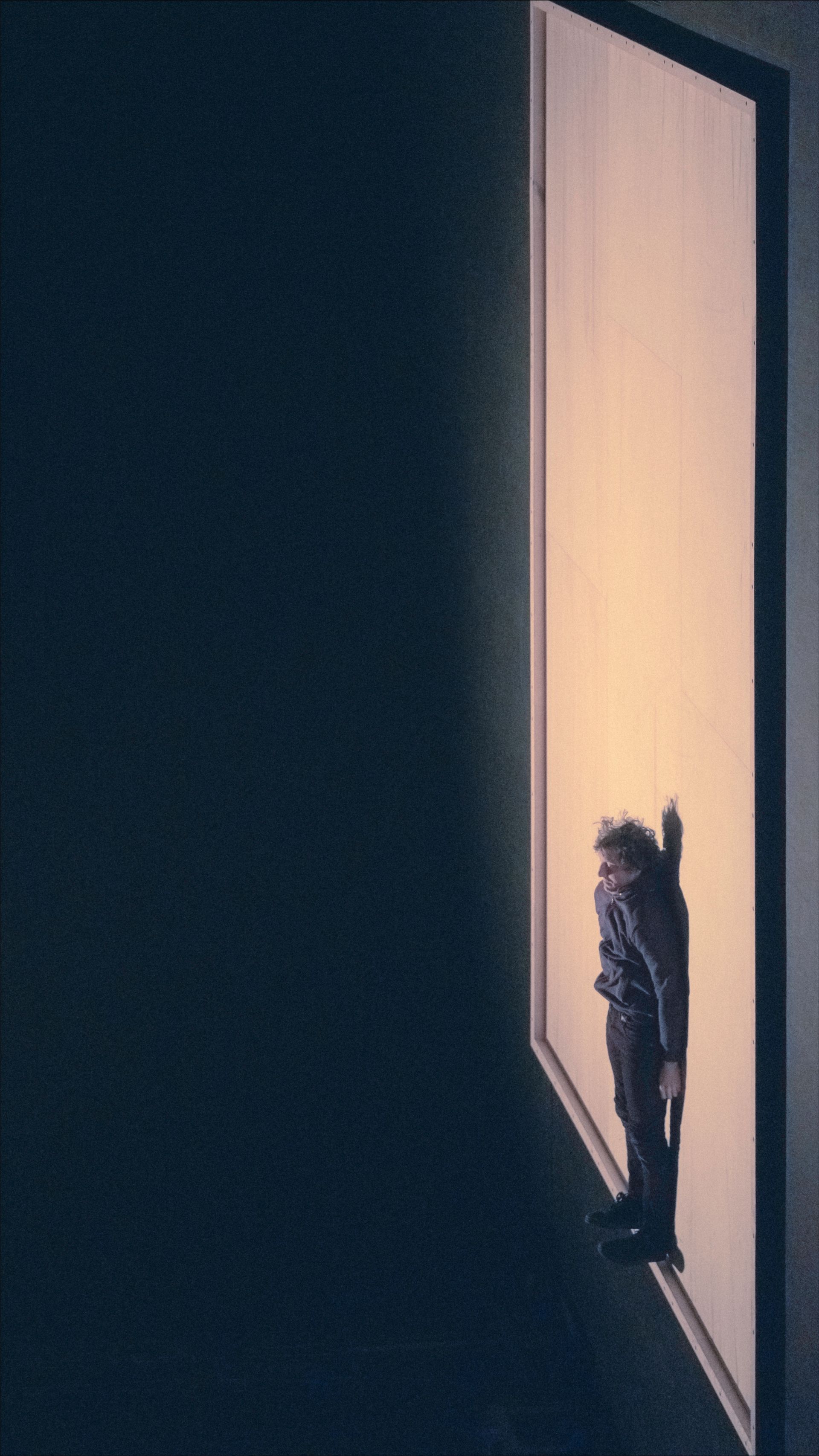 Person standing in a brightly lit doorway, looking out. Dark room to the left.